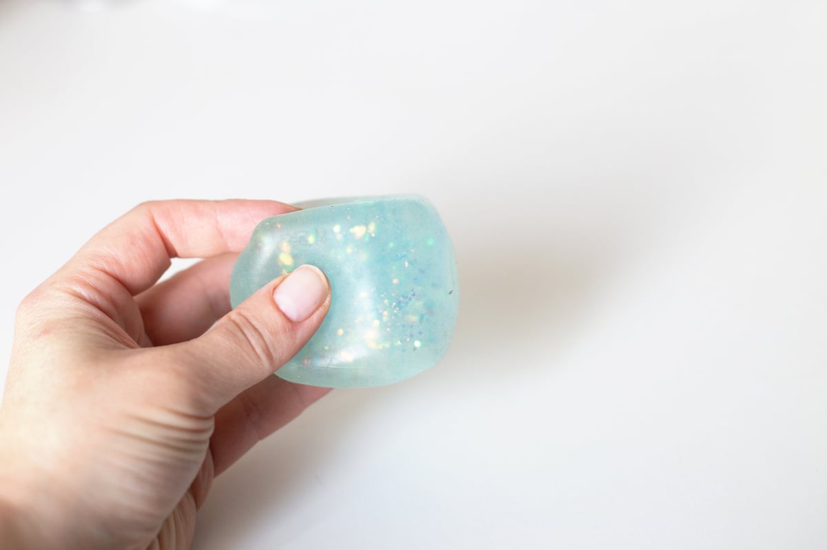 Hand holding and deforming a light blue squishy toy with glitter